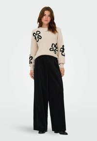 Cream-colored sweater with black flower appliqués, paired with wide black corduroy pants. Smooth texture, relaxed fit, long sleeves.