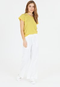 Gul kortærmet skjorte, afslappet pasform, parret med løstsiddende hvide linnedbukser. Modellen har hvide sneakers på. Enkel design, ingen mønstre.