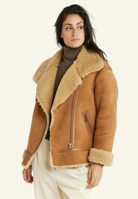 Bruine suède jas met een beige nepbont kraag en manchetten, voorzien van een zijrits en een strak ontwerp. Zachte textuur en een ontspannen pasvorm.