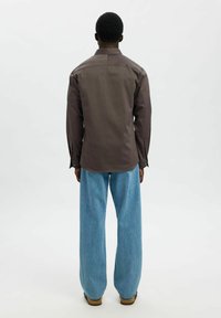Brun långärmad skjorta med rak skärning, som har en subtil lyster och knäppta manschetter, i kombination med överdimensionerade ljusblå jeans.
