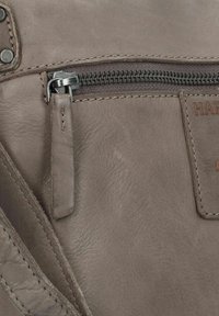 Sezione di borsa in pelle grigia con una tasca con cerniera dotata di un cursore in metallo e una cucitura di accento color tabacco lungo il bordo.