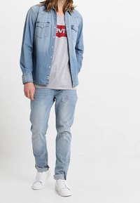 Světle modrá denimová košile se sepnými knoflíky přes šedé tričko Levi's. Oblečení doplňují světle modré džíny a bílé tenisky.