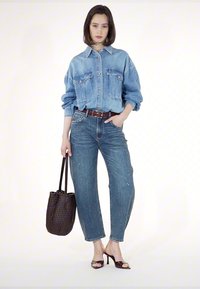 Denim oversize jakna z dvema sprednjima žepoma, svetlo modri traperji s bleščicami, rjav pas, vzorčasta črna torba in sandali z odprtimi prsti.