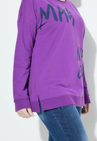 Maglietta lunga viola con maniche cadenti, caratterizzata da una stampa audace in verde scuro. Fessure laterali all'orlo e un design dalla vestibilità rilassata.