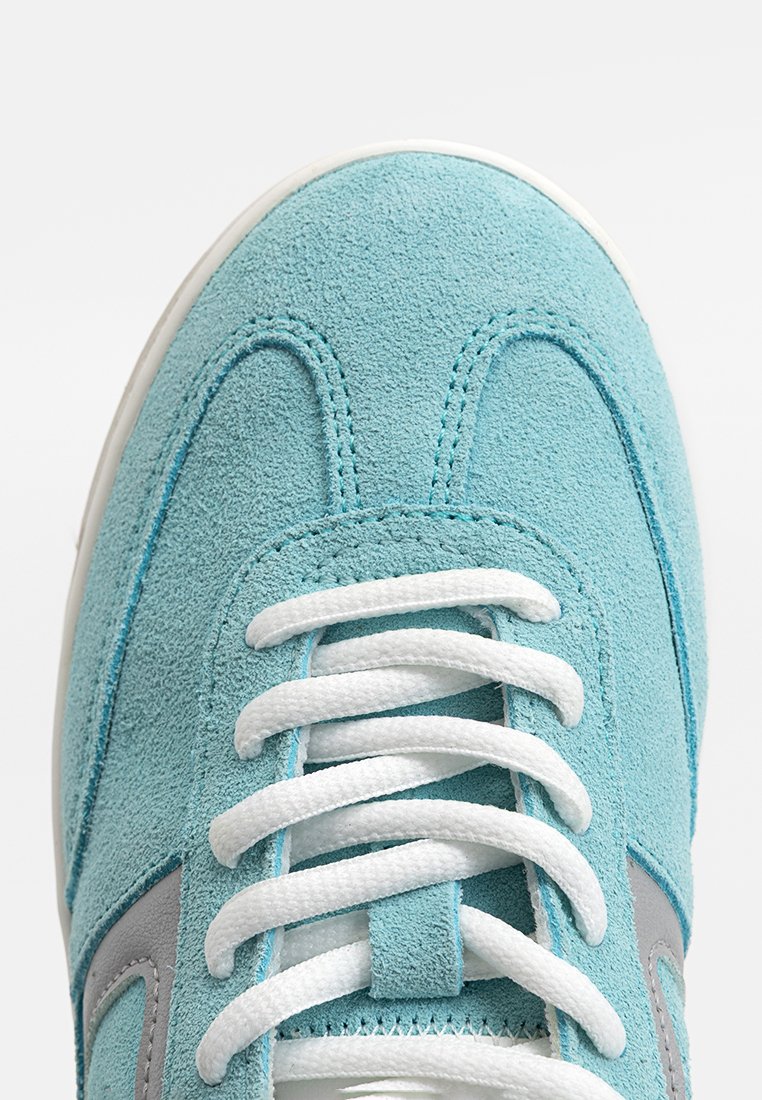 Zapatilla de gamuza azul claro con cordones blancos, acentos grises en los laterales y puntera redondeada. Superior texturizado con detalles de costura.