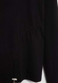 Chemise en coton noire à coupe décontractée, dotée d'une poche latérale et d'un détail de ventilation. L'ourlet est orné d'un accent en métal argenté.