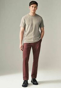 Camiseta gris de manga corta combinada con pantalones slim-fit burdeos. El modelo lleva zapatos negros de cordones. Textura de tela suave, diseño casual.
