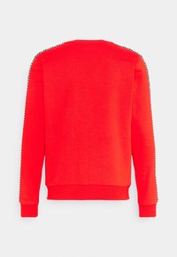 Sweatshirt rouge avec un col rond et des manches longues. Présente une bordure noire et blanche le long des coutures latérales. Texture douce et design décontracté.