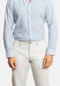 Camisa a rayas, principalmente en azul claro y blanco, con cuello abotonado y mangas largas. Combinada con pantalones de color claro.