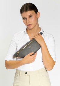 Grau texturiertes Slingbag mit einem goldenen Reißverschluss, eng am Körper gehalten. Verfügt über ein schlankes Design und einen verstellbaren Tragegurt.