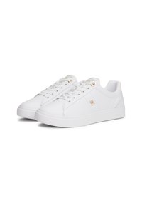 Paire de baskets basses blanches avec lacets à l'avant et petit logo doré sur le côté, présentées sur fond blanc.
