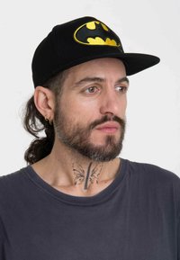Black cap featuring a large yellow Batman logo on the front. The cap has a flat brim and is made from fabric with a smooth texture.