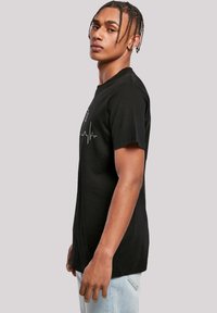 Black cotton t-shirt with short sleeves, featuring a heartbeat graphic in white on the front. Standard fit, smooth texture.
