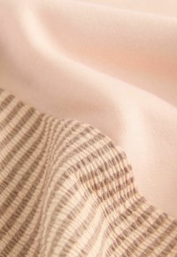 Stickad tyg med en solid ljusrosa sektion och ett randigt mönster i beige och kräm. Mjuk textur med synliga vävdetaljer.
