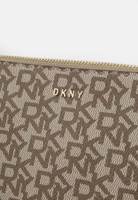 Brązowa saszetka z logo DKNY w kolorze złotym. Powierzchnia ma teksturowany wzór z nachodzących na siebie liter, z złotym zamkiem błyskawicznym na górze.