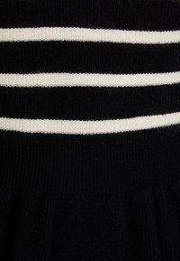 Svart strikket kjole med horisontale hvite striper. Ribbet tekstur på toppen, utvidet bunndel. Mykt stoff, midtlengde design.