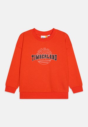 Punainen puuvillapaita pitkillä hihoilla, ribbehäntäisillä ompeleilla ja pyöreällä kaula-aukolla. Edessä mustavalkoinen "TIMBERLAND"-logo.