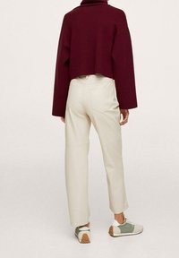 Gekürzter burgunderfarbener Pullover, cremefarbene Hose mit Gesäßtaschen und graue Sneaker mit grünen Akzenten. Weicher Stoff und entspannte Passform.