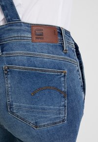 Denimbyxor i ljusblått med en brunt läderlogga, synlig sömnad och en bakficka med en kurvad design.