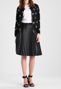 Svart bomberjacka med blommig broderi, kombinerad med en svart plisserad kjol i konstläder och svarta klackskor med ankelrem.