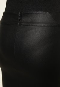 Jupe en cuir noir avec une texture lisse, un design ajusté, une taille haute et des détails de coutures discrets.