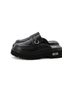 Scarpe slip-on nere con piattaforma realizzate in pelle liscia, dotate di una fascia con un anello metallico, suola texturizzata e un'accento con il marchio sul lato.