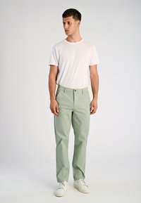 Jasnozielone, proste spodnie z guzikowym zapięciem, kieszeniami z przodu oraz gładką bawełnianą teksturą, noszone z gładką białą koszulką i białymi sneakersami.