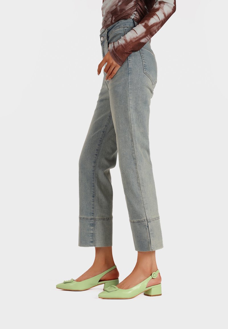 Jeans in denim leggero blu chiaro a vita alta con gambe cropped, caratterizzati da orli grezzi. Abbinati a scarpe slingback verde menta con un dettaglio a fiocco.