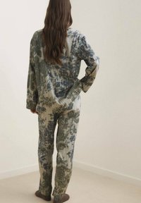 Conjunto de ropa de estar de tie-dye en tonos verdes y beis, con un corte relajado, textura acanalada y mangas largas. Diseño simple y casual.
