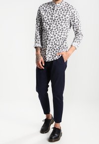 Valkoinen nappipaita, jossa musta lehtikuvio, pitkät hihat, yhdistetty laivastonsinisiin housuihin ja mustiin kenkiin, esittäen istuvan siluetin.