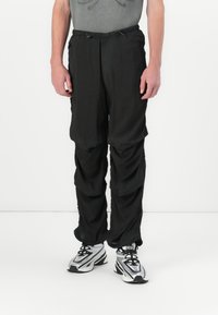 Pantalons légers noirs à coupe ample, dotés d'une taille élastique et d'un cordon de serrage, de coutures froncées et d'une texture lisse.