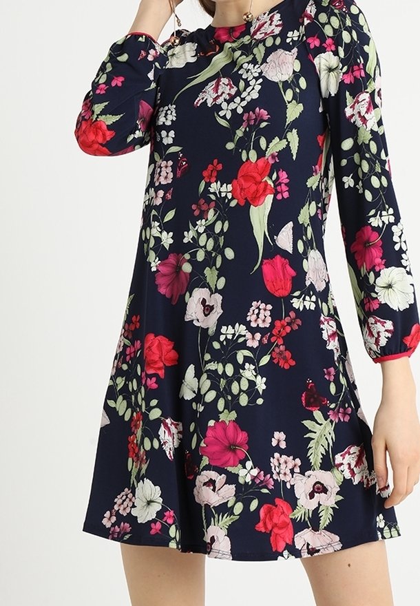 Kukallinen pitkähiha dressi tummansinisellä pohjalla, jossa on erilaisia eläviä kukkia. Mekko on väljää mitoitusta ja valmistettu pehmeästä, sileästä kankaasta.