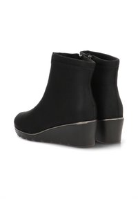 Botas de tobillo negras de tejido suave, con tacón en cuña, cierre de cremallera y diseño minimalista sin patrones visibles.