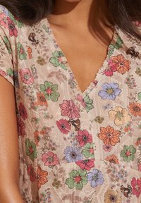 Vestido floral con escote en V y mangas cortas. El material es ligero, con un fondo beige, adornado con patrones florales coloridos.
