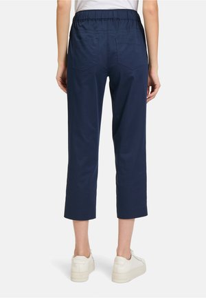 Pantaloni cropped blu navy con vita elasticizzata, due tasche posteriori e texture liscia. Indossati con sneakers bianche per un contrasto.
