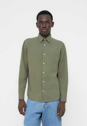 Chemise à manches longues vert olive avec col boutonné et boutons sur le devant, associée à un jean en denim bleu clair.