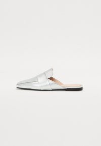 Sølvmetalliske slip-on sko med teksturert overflate, spiss tå og bred stropp over låret. Flat såle, minimalistisk design.