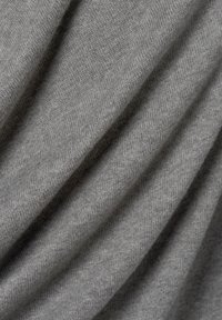 Grau gestrickter Stoff mit einer weichen Textur, der subtile diagonale Linien und unterschiedliche Schattierungseffekte durch Drapierung zeigt.
