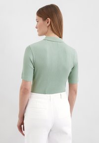 Ribbed, rövidujjú póló világos zöld színben, gallérral. Magas derekú fehér nadrággal párosítva. Sima textúra, testre simuló dizájn.