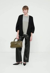 Μαύρη πλεκτή ζακέτα, γκρι μπλουζάκι, μαύροι παντελόνες από συνθετικό δέρμα, μυτερά μαύρα παπούτσια, κρατώντας μια ελιά πράσινη τσάντα με έμφαση αστεριού.