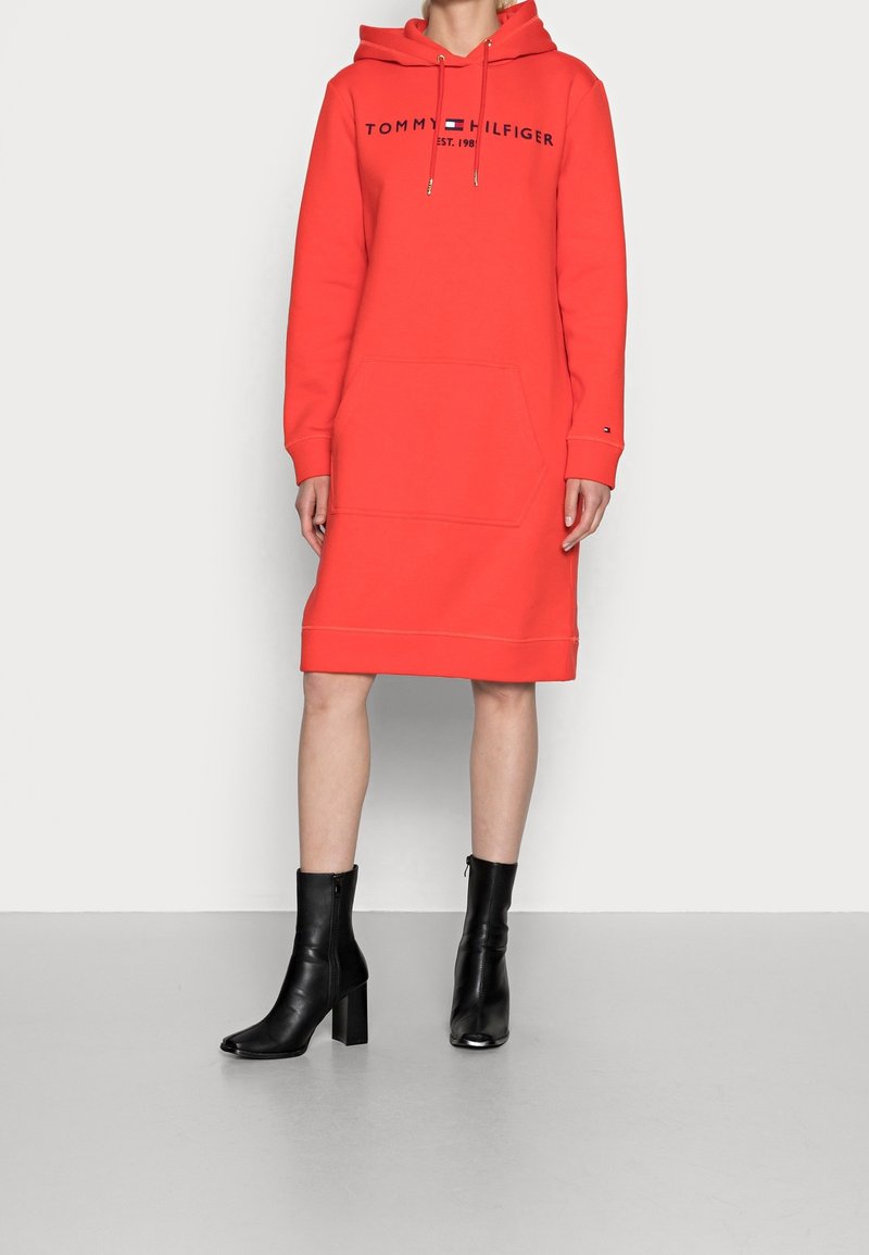 Röd huvtröjklänning med logotyp, framficka och ribbad slutning, kombinerad med svarta ankelskor med hög klossklack.