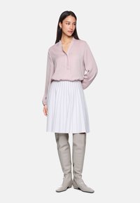 Light pink long-sleeve blouse with a V-neck, paired with a white pleated skirt and knee-high beige boots. Smooth fabric and structured design.