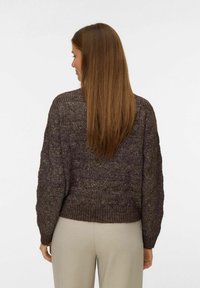 Maglione a maglia marrone con texture, orlo a coste e vestibilità ampia, caratterizzato da un motivo sottile. Il modello indossa pantaloni chiari.