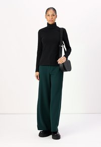 Must must-särgmine turtleneck, tumesinised laiad püksid, mustad jämedad jalanõud ja väike must õlakott, millel on reljeefne logo detail.