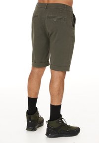 Khakishorts med uppvikta fållar, med bakfickor med knappstängning. Bärs med svarta strumpor och vandringssandaler.