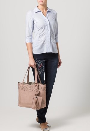 Lichtblauw overhemd met knopen, donkere spijkerbroek en een beige geperforeerde shopper met een kwastje, voorzien van gedetailleerde bovenrand. Zilveren ballerina's maken de outfit compleet.
