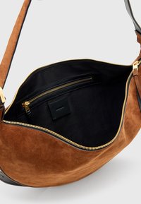Borsa a spalla in suede marrone con una sola tracolla, chiusura con zip dorata e fodera interna nera che presenta una piccola tasca con zip e il marchio.