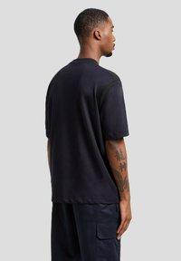 T-shirt nero a maniche corte con dettagli verde sulle spalle, realizzato in tessuto morbido. Presenta una vestibilità comoda e un orlo dritto.