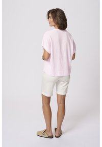 Blouse courte à manches courtes de couleur rose clair en lin, associée à un short blanc à mi-cuisses et des chaussons beiges. Conception simple et décontractée.