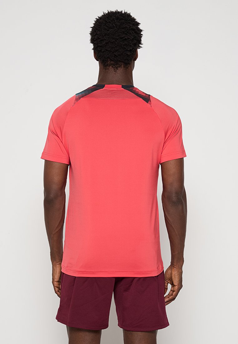 T-shirt de sport rouge à manches courtes avec une texture lisse. Présente des détails noirs sur le haut du dos et des manches raglan.